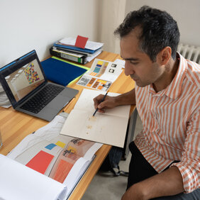 Der Künstler Rozbeh Asmani sitzt am Schreibtisch und arbeitet an einem Entwurf.