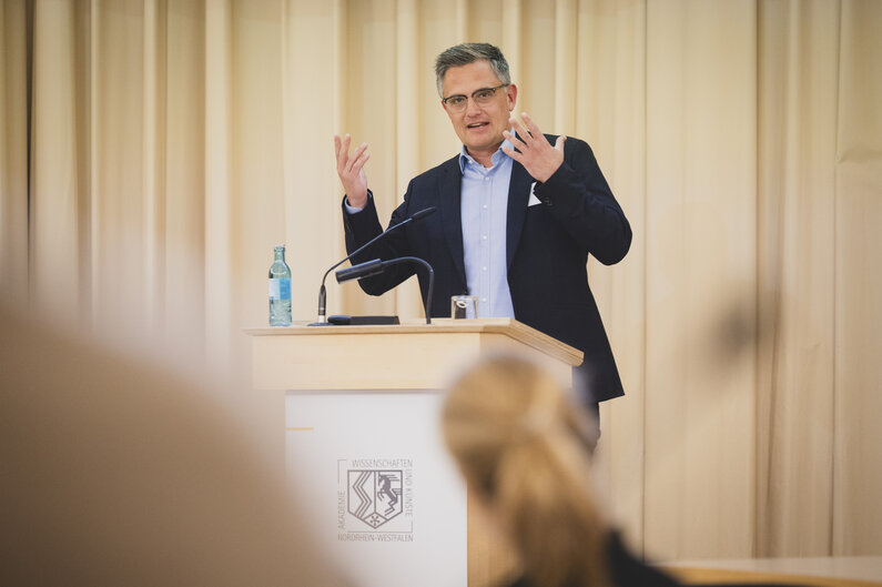 Ein Mann steht an einem Rednerpult. Er gestikuliert mit den Händen.