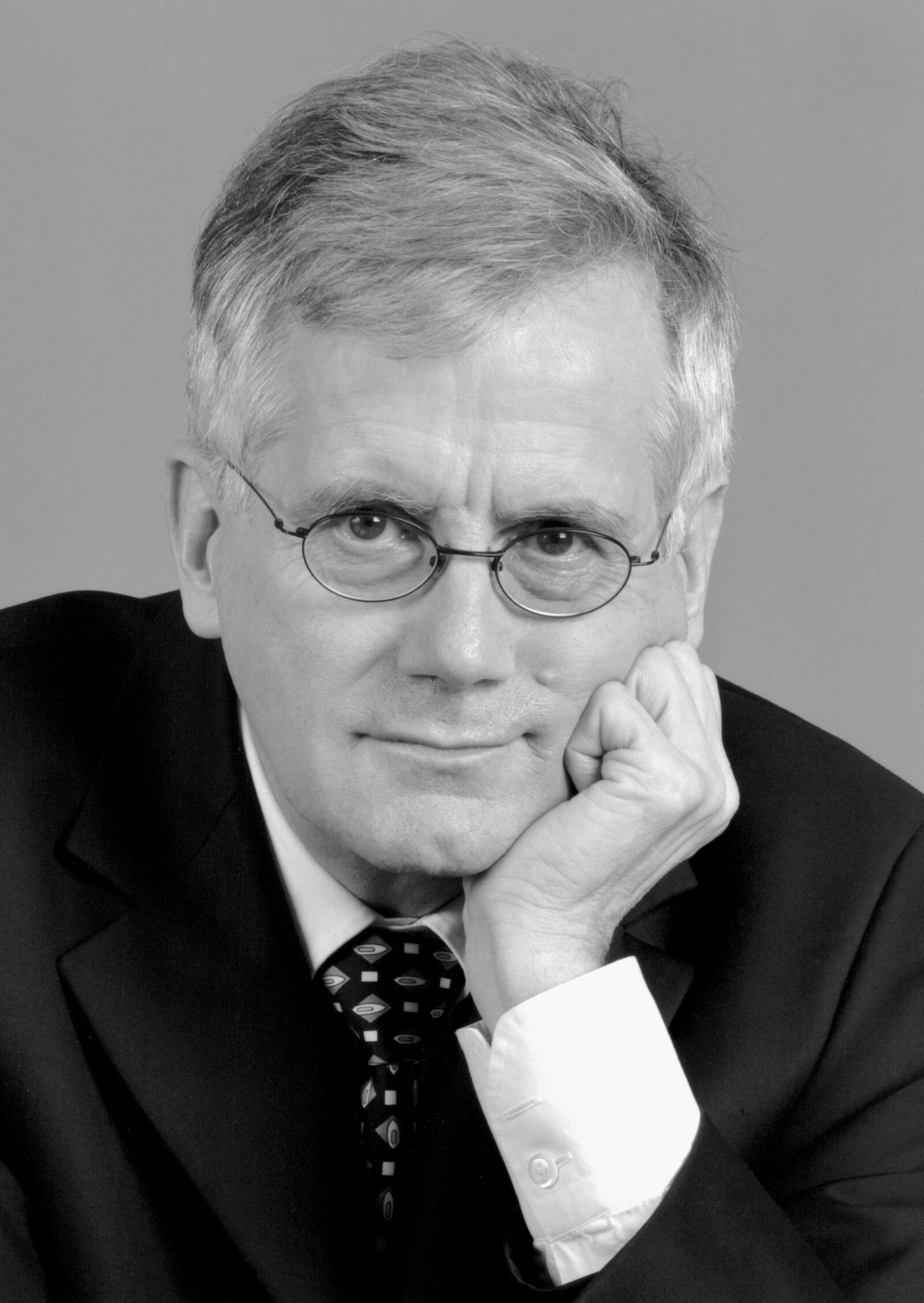 Ein Mann mit Brille stützt sich auf seine linke Hand. Er lächelt in die Kamera.