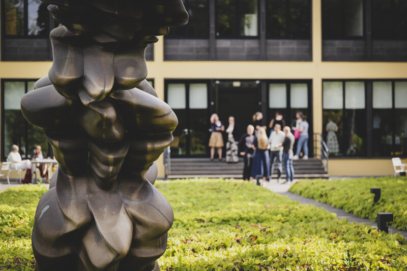 Junge Menschen stehen im Garten der Akademie und unterhalten sich. 