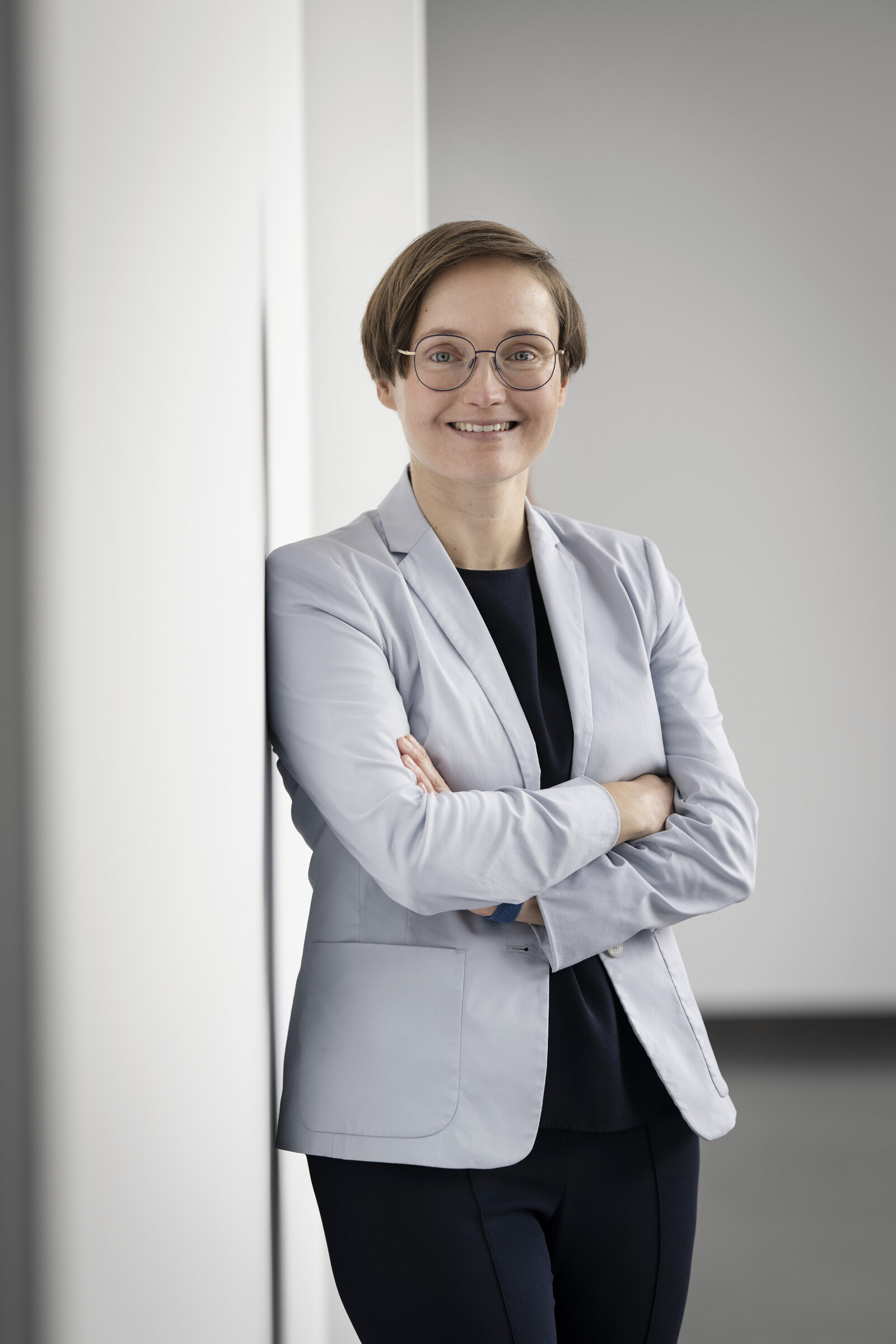 Eine Frau lehnt an einer weißen Wand. Sie lächelt in die Kamera.