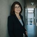 Frau mit Brille lehnt lächelnd an einer Wand.