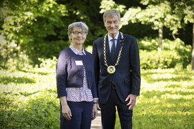 Eine Frau und ein Mann stehen in einem Park und lächeln in die Kamera.
