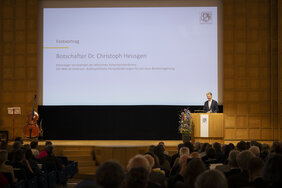 Ein Mann steht an einem Rednerpult. Im Hintergrund ist sein Name eingeblendet: Botschafter Dr. Christoph Heusgen.