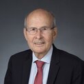 Ein Mann mit Brille trägt eine Krawatte und eine ANzugkacke. Er lächelt in die Kamera.
