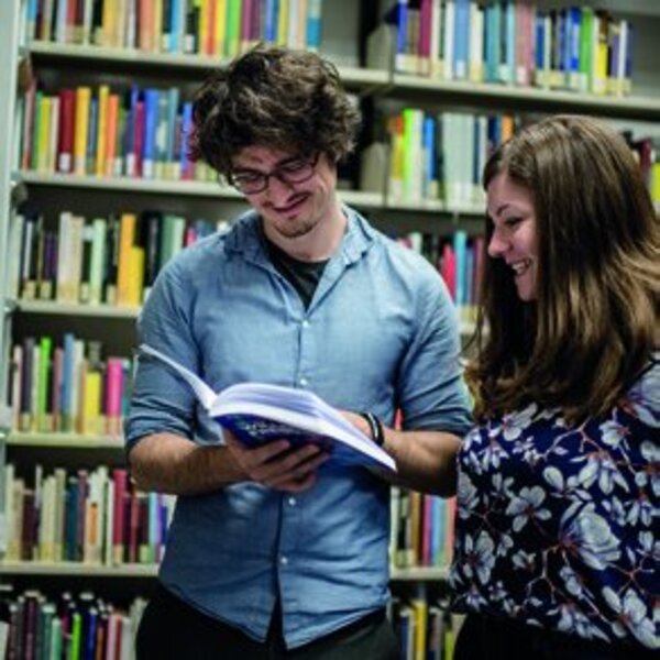 Zwei Menschen schauen gemeinsam in ein Buch in der Bibliothek