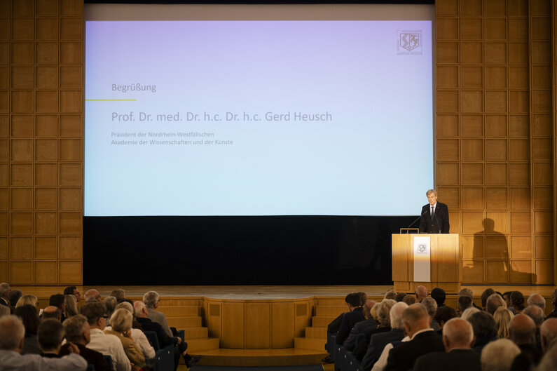 Ein Mann steht an einem Rednerpult. Im Hintergrund ist sein Name eingeblendet: Prof. Dr. med. Dr. h.c. Dr. h.c. Gerd Heusch