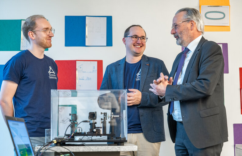 Drei Männer stehen um einen Tisch herum, auf dem ein technisches Gerät platziert ist.