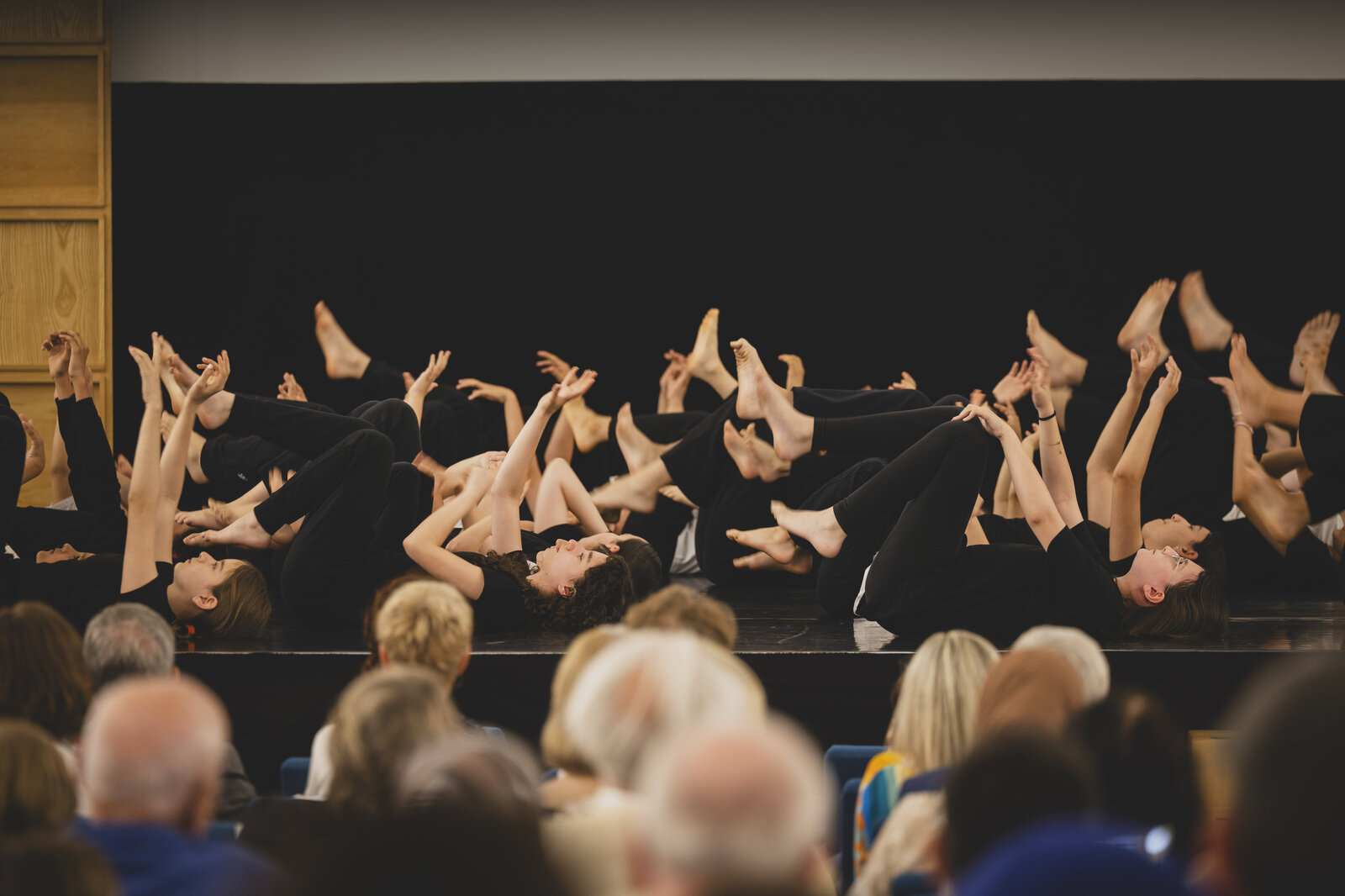 Mädchen und Jungen in schwarzer Kleidung liegen auf dem Boden und strecken die Arme und Beine in die Luft.
