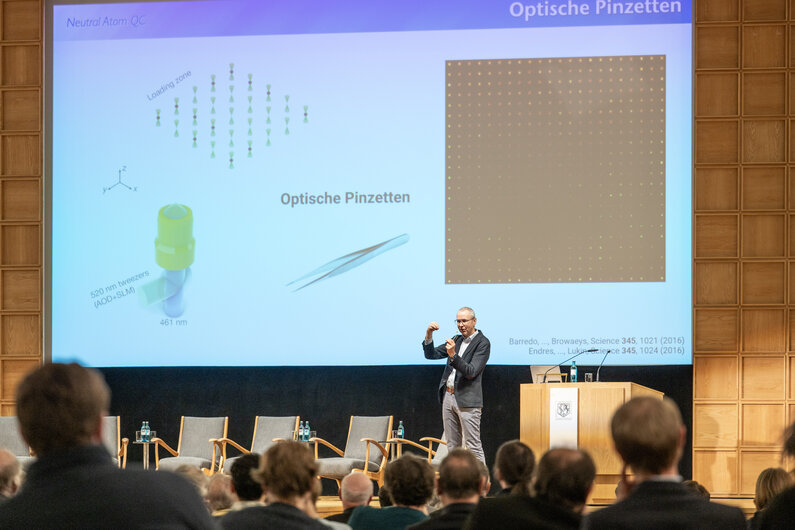 Ein Mann steht auf einer Bühne. Er hält einen Vortrag über Optische Pinzetten. 
