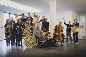 Musikerinnen und Musiker mit verschiedenen Instrumenten spielen im Gartenfoyer der Akademie.