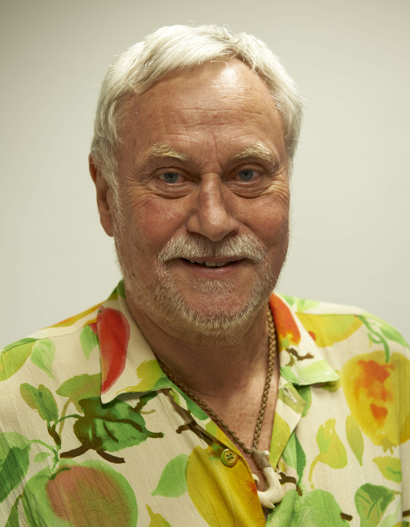 Ein Mann mit Bart trägt ein buntes Hemd. Er lächelt in die Kamera.