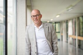 Porträt Professor Dr. Joost-Pieter Katoen. Der Informatiker steht in einem langen Flur und blickt in die Kamera.