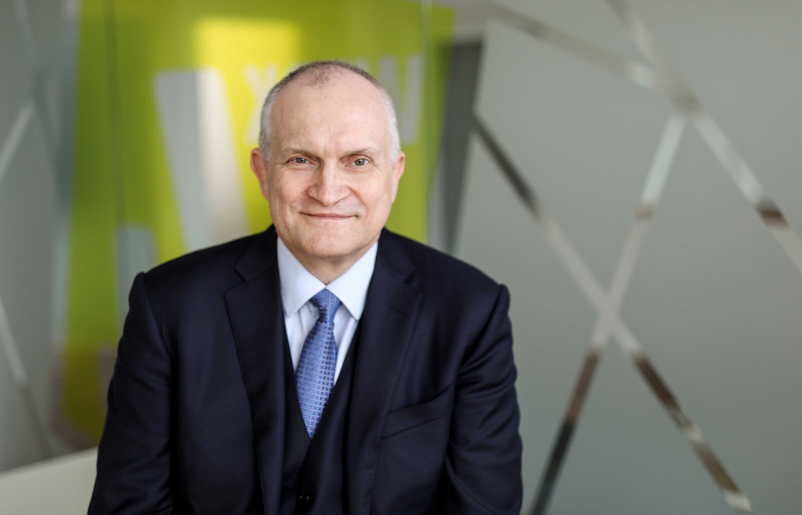 Mann steht lächelnd vor einem Kunstwerk.