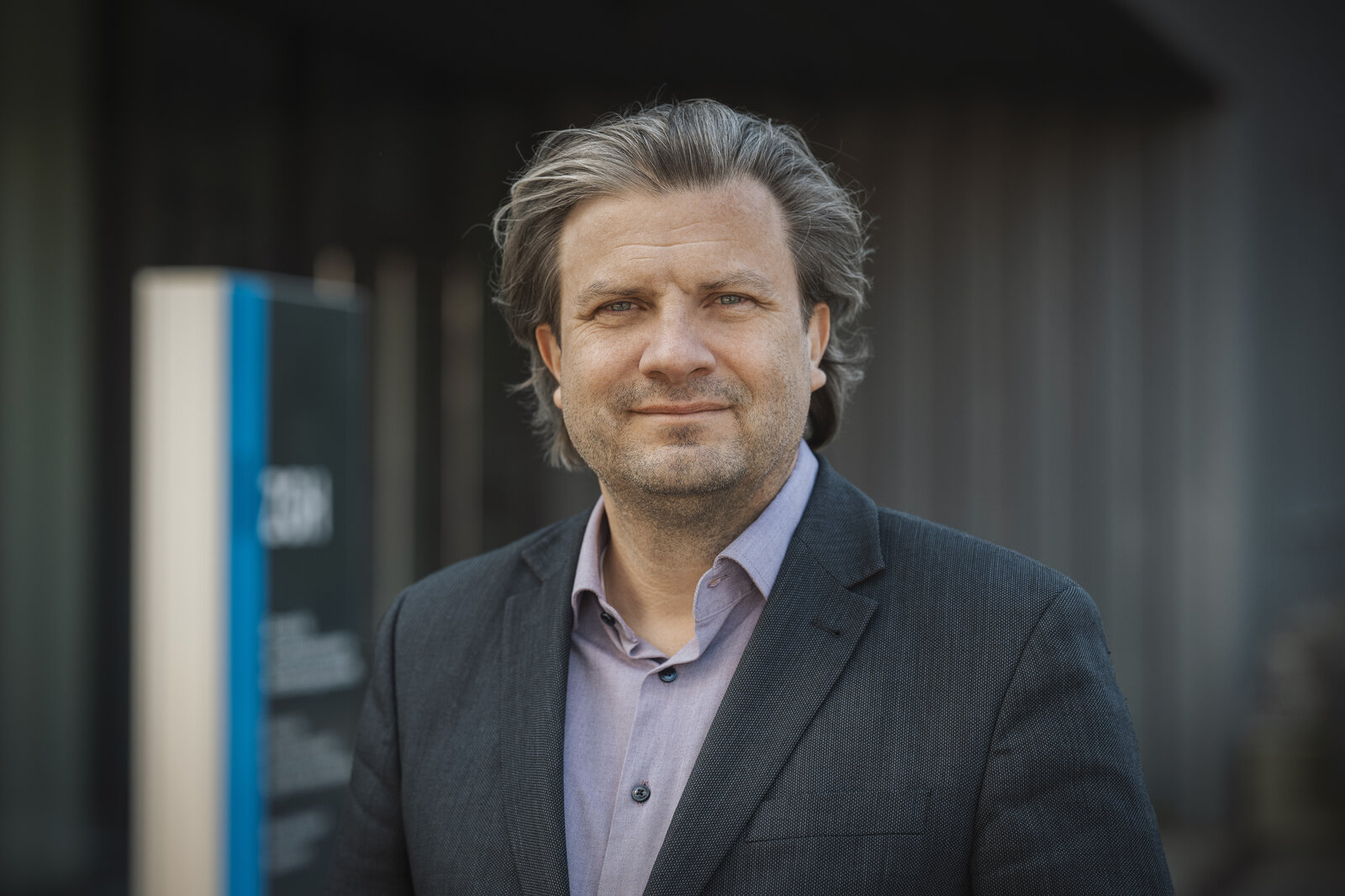 Ein Mann trägt eine Anzugjacke und lächelt in die Kamera.