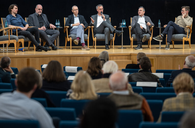 Auf einem Podium sitzen sechs Männer.