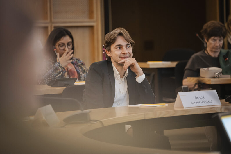 Ein Mann sitzt in einem Vortragsraum. Auf dem Tisch vor ihm steht ein Schild mit seinem Namen "Dr.-Ing. Lorenz Dörschel".
