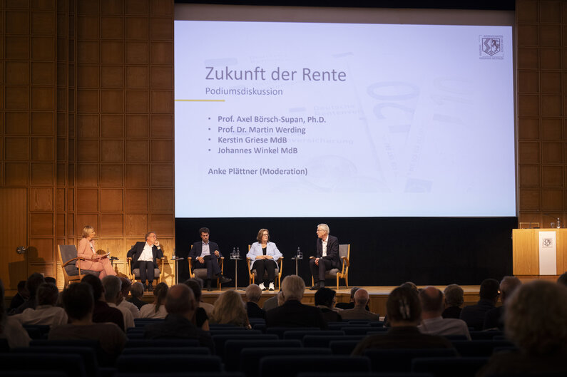Zwei Frauen und drei Männer sitzen auf einem Podium. Auf der Leinwand hier ihnen ist der Titel der Veranstaltung eingeblendet: Zukunft der Rente.