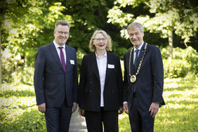 Eine Frau und zwei Männer haben sich in einem Park für ein Foto aufgestellt.
