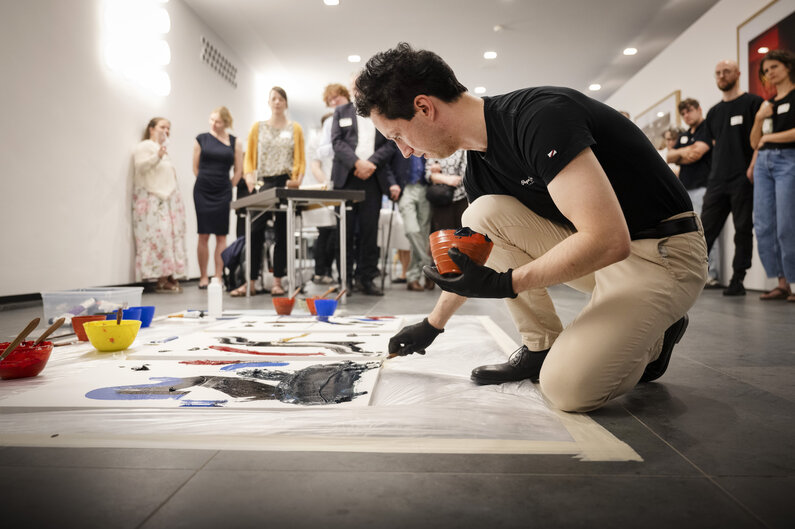 Ein Mann malt auf dem Boden ein großflächiges Kunstwerk.