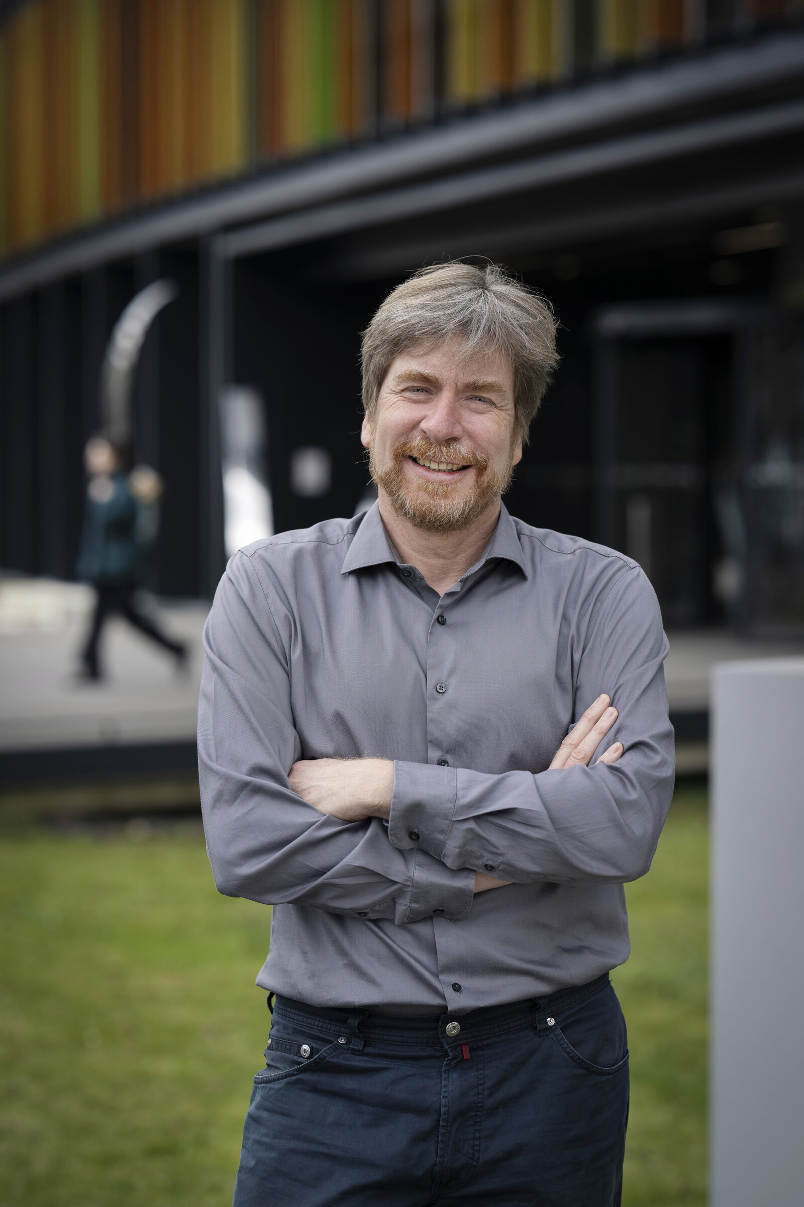 Ein Mann in einem grauen Hemd lächelt in die Kamera. 