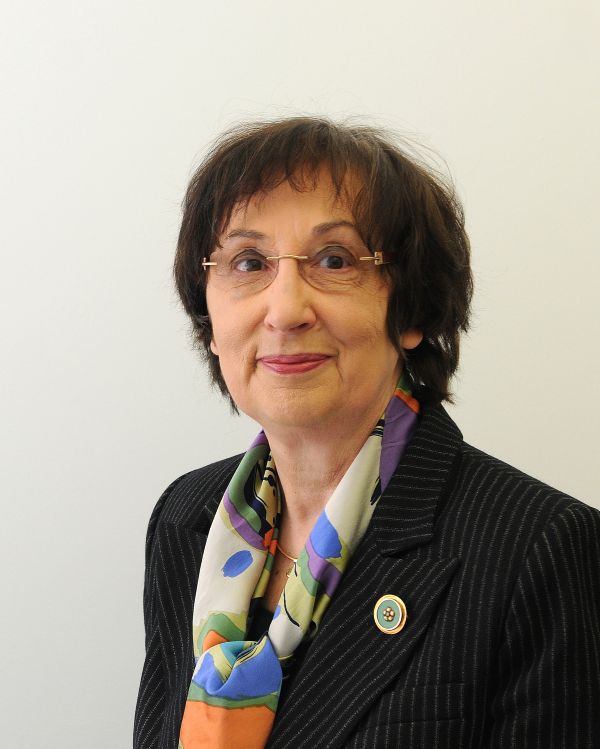 Eine Frau mit Brille lächelt in die Kamera. Sie trägt ein buntes Halstuch zu einer Anzugjacke.