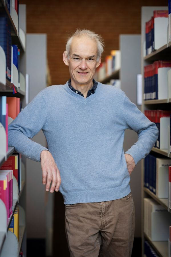 Ein Mann lehnt lächelnd an einem Bücherregal.