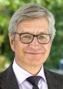 Ein Mann mit schwarzer Brille lächelt freundlich in die Kamera. 