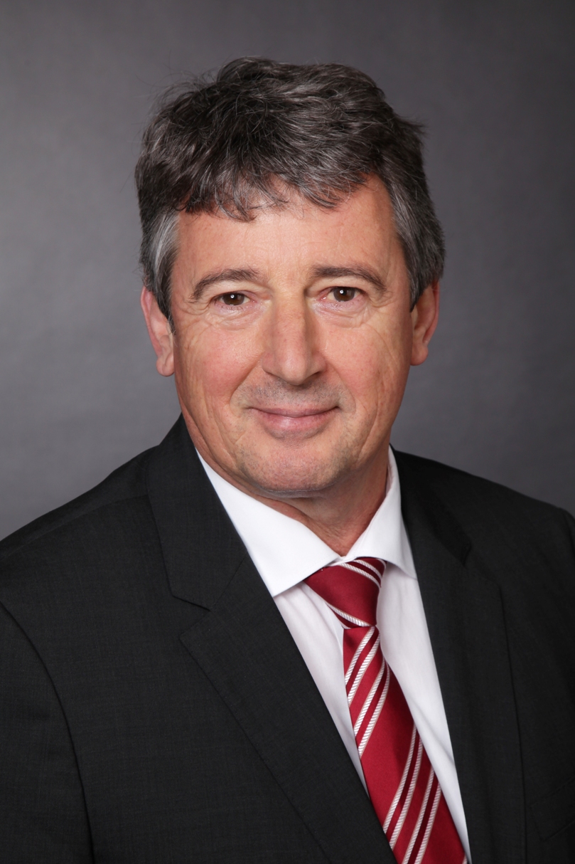 Ein Mann in Anzugjacke und mit Krawatte schaut lächelnd in die Kamera.