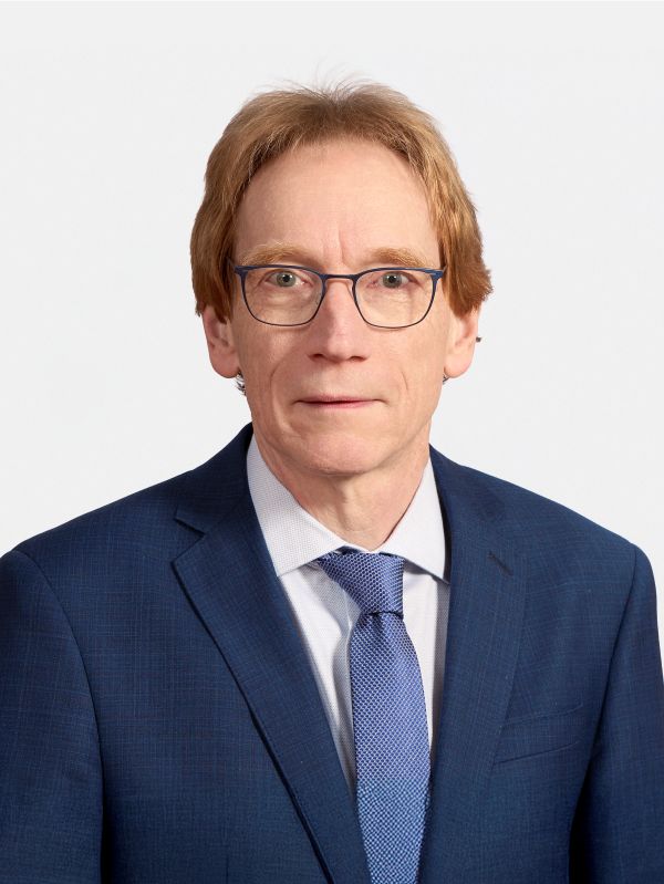 Ein Mann mit Brille schaut freundlich in die Kamera. Er trägt eine Krawatte und eine Anzugjacke.