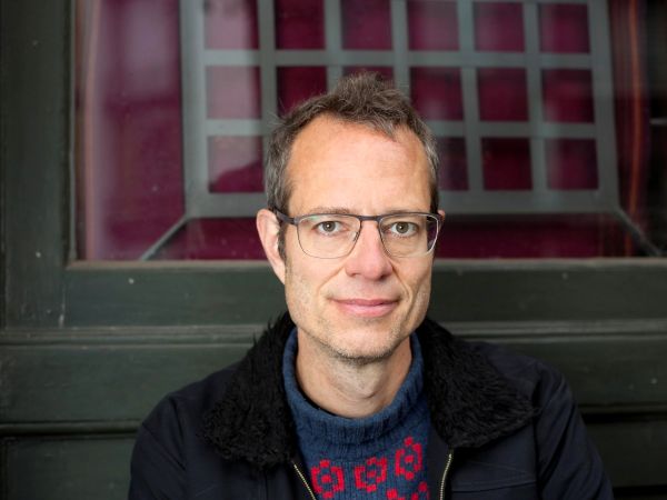 Ein Mann mit Brille steht lächelnd vor einem Fenster.