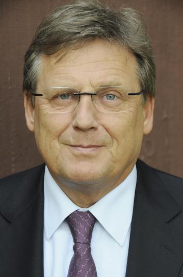 Ein Mann mit Brille schaut freundlich in die Kamera. Er trägt eine Krawatte.