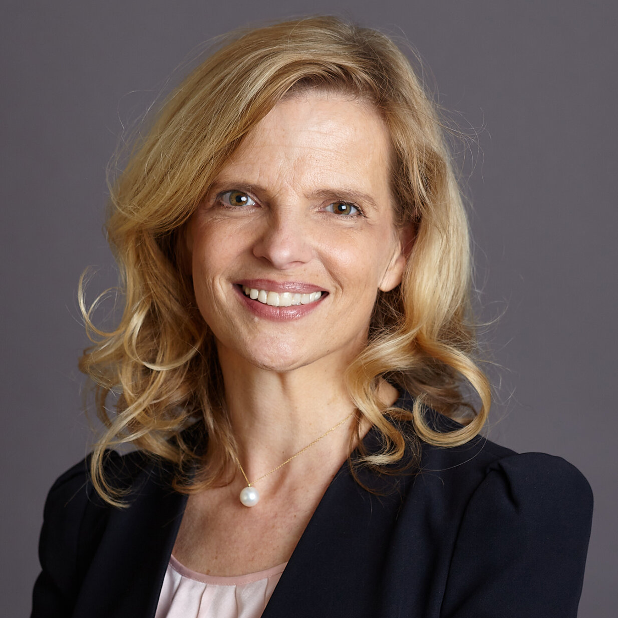 Eine Frau mit schulterlangen Haaren lächelt strahlend in die Kamera.