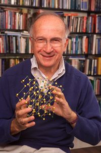 Ein Mann sitzt vor einem Bürcherregal und hält lächelnd ein chemisches Modell in den Händen.