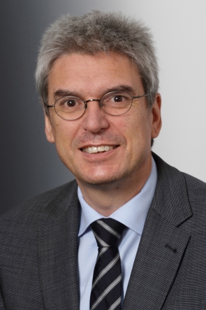 Ein Mann mit Brille und Krawatte lächelt in die Kamera.